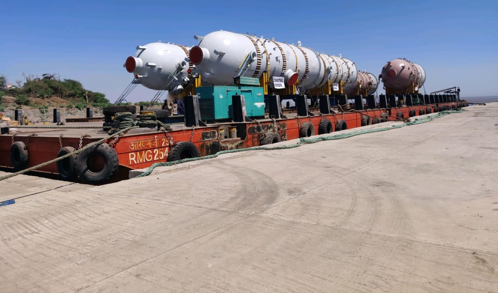 A line of process vessels secured on a barge deck at the jetty — coastal movement used where the road corridor cannot take the envelope.