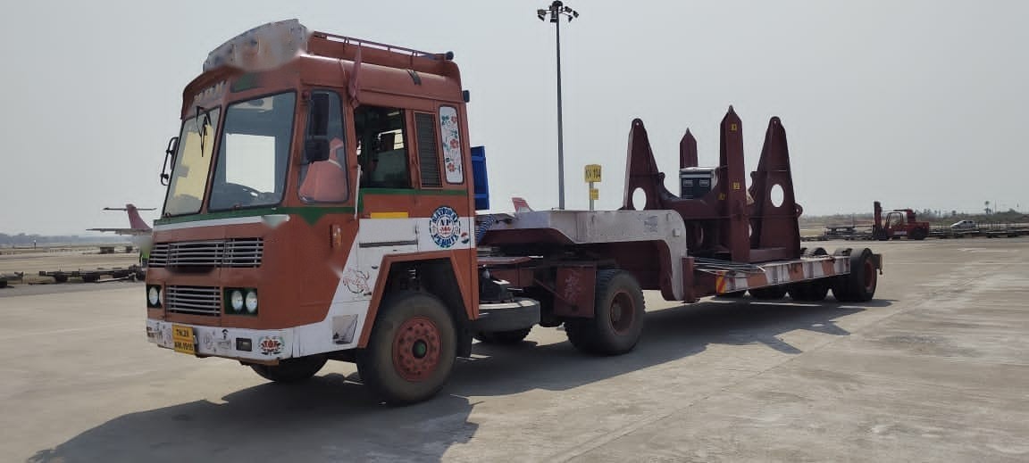 A tractor coupled to a low bed rigged with steel saddles, staged on an apron and ready to receive its load.