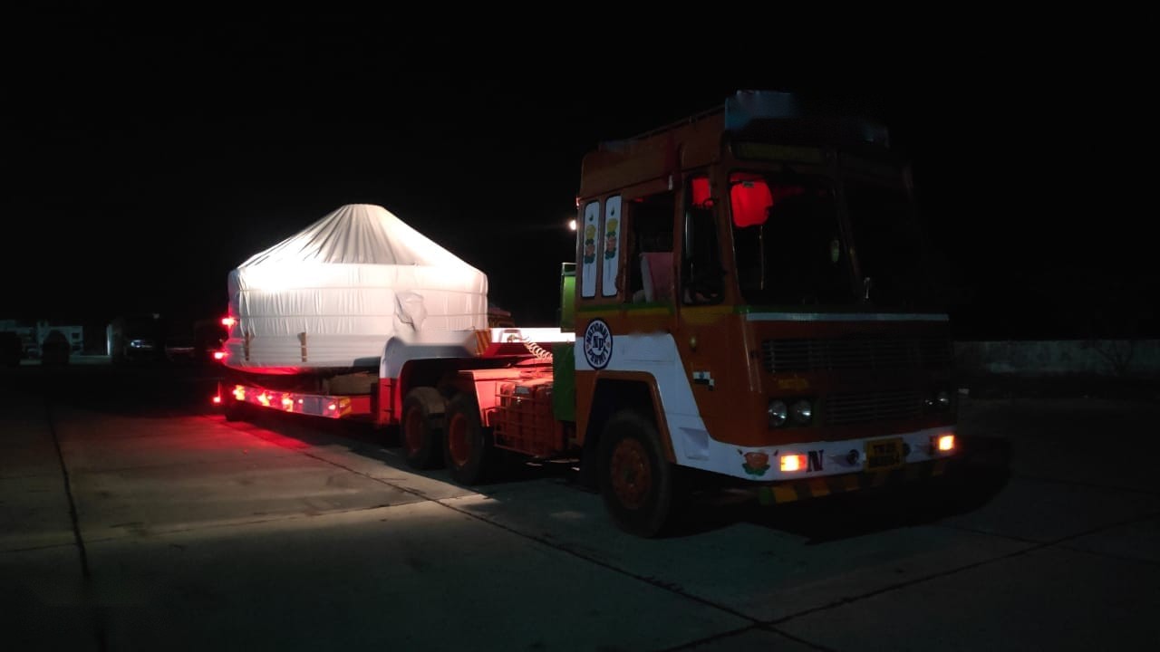 Shrink-wrapped cargo on a low bed under marker lights. Restricted-hour running keeps oversized loads off congested corridors during the day.
