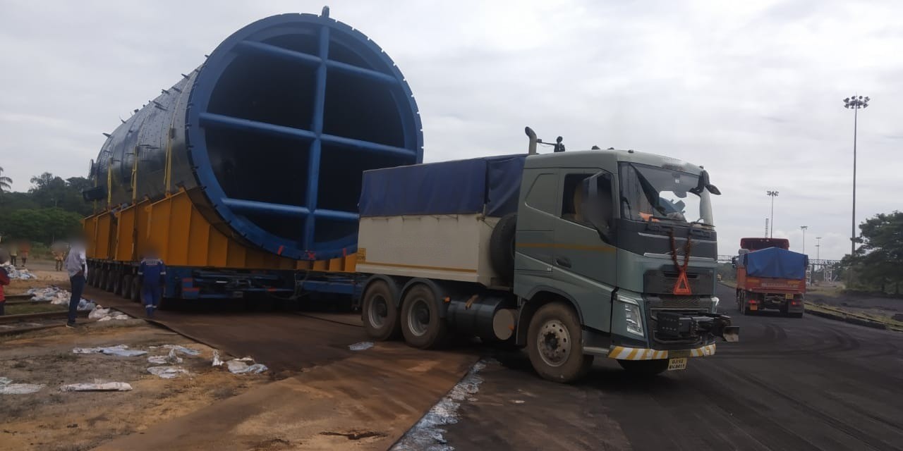 A blue large-diameter vessel on hydraulic axle lines being drawn out of a port rail yard by a heavy prime mover