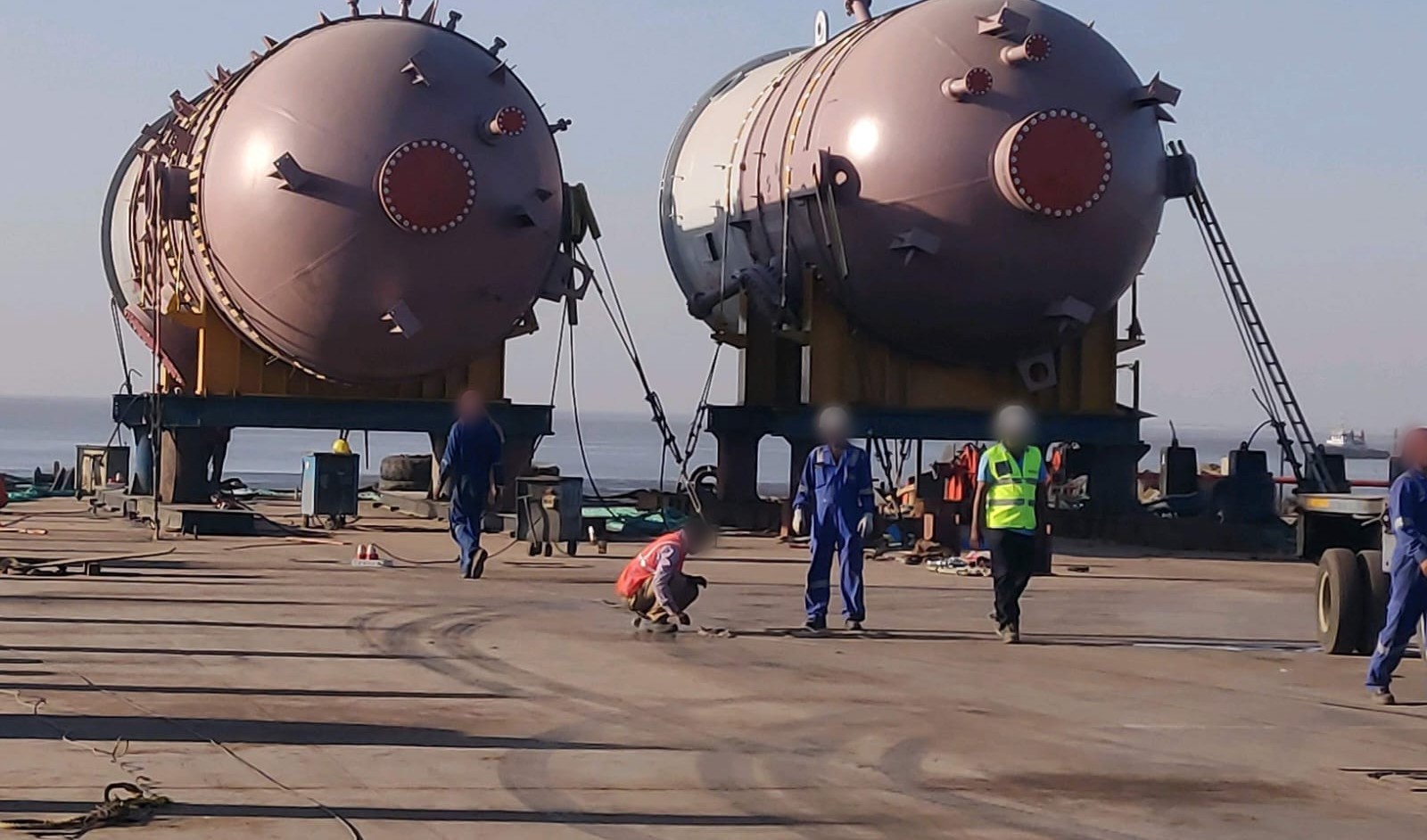 Crew in hard hats and high-visibility clothing preparing reactor vessels for transfer at a jetty
