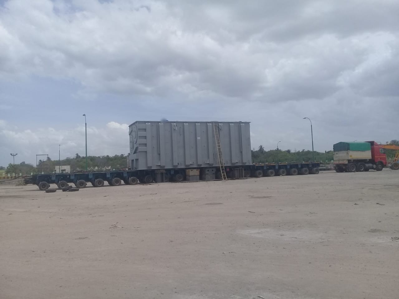 A power transformer tank on a long multi-axle hydraulic trailer in an open port stacking yard